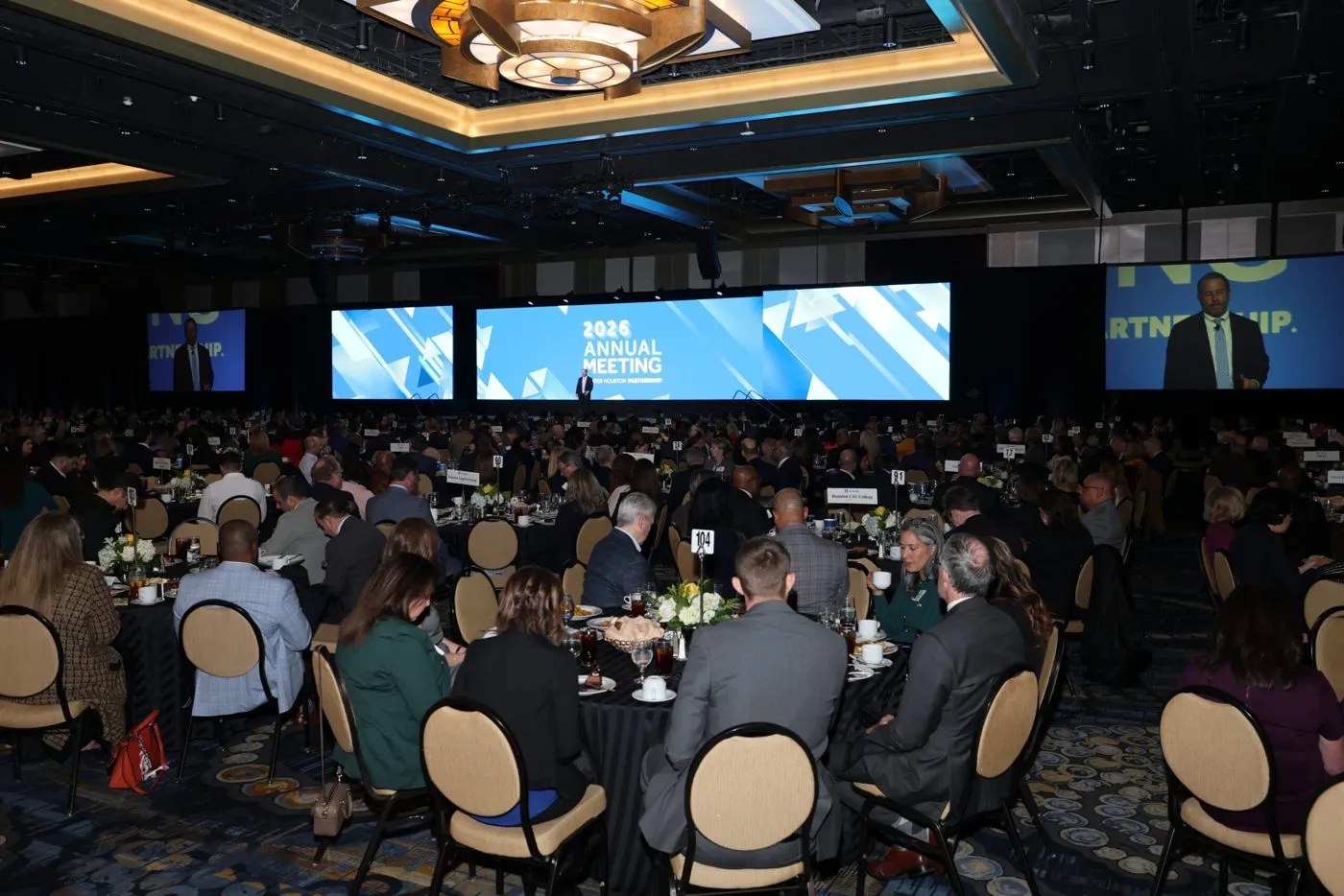 Seated audience in a large corporate meeting room with wide screens