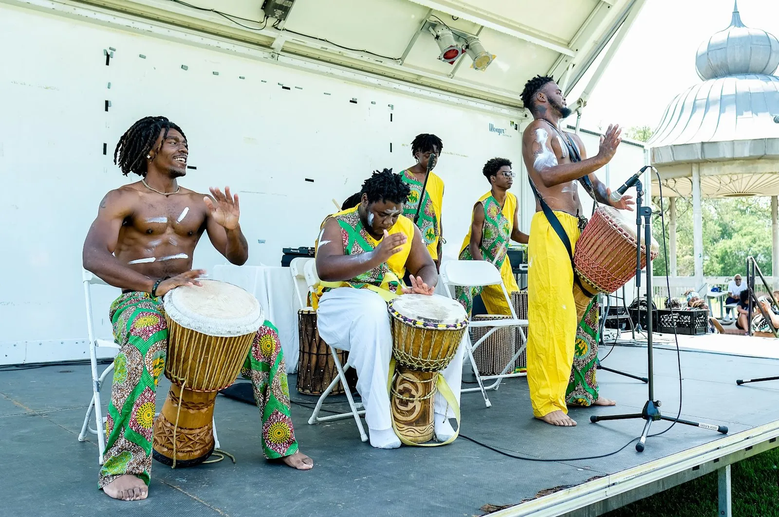 Drummers and a musician performing on an outdoor stage