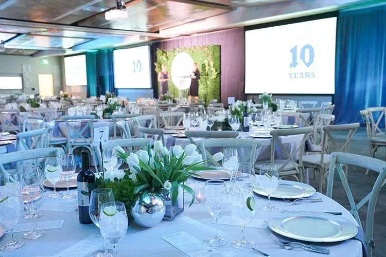Banquet room set with floral centerpieces and screens reading '10 Years'