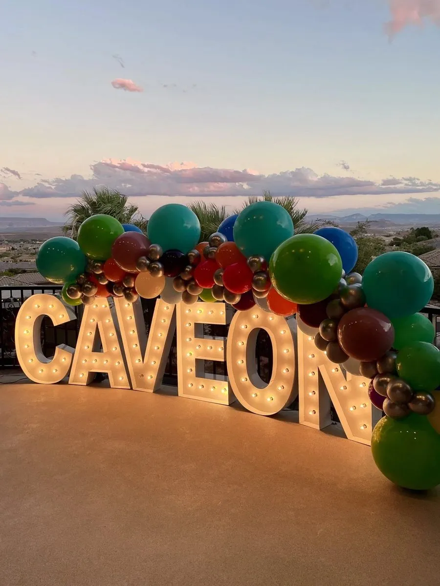 Lit CAVEON letters with a balloon garland at sunset