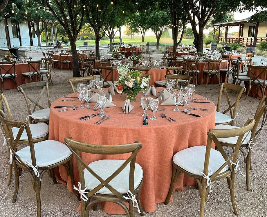 Round tables set for an outdoor group dinner under trees