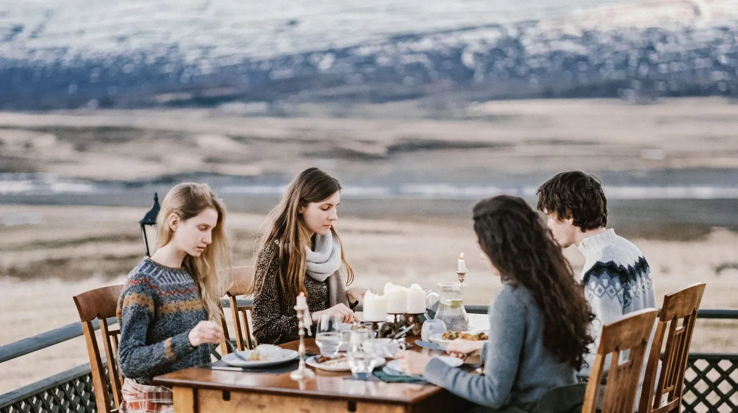 Four people share a meal at a wooden table on a terrace with snow-capped mountains behind them during an all-inclusive corporate retreat.