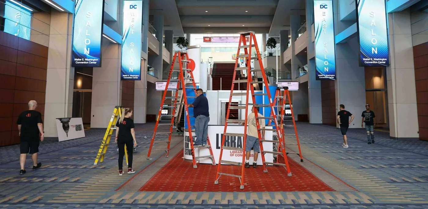Production crew setting up a convention center concourse with ladders
