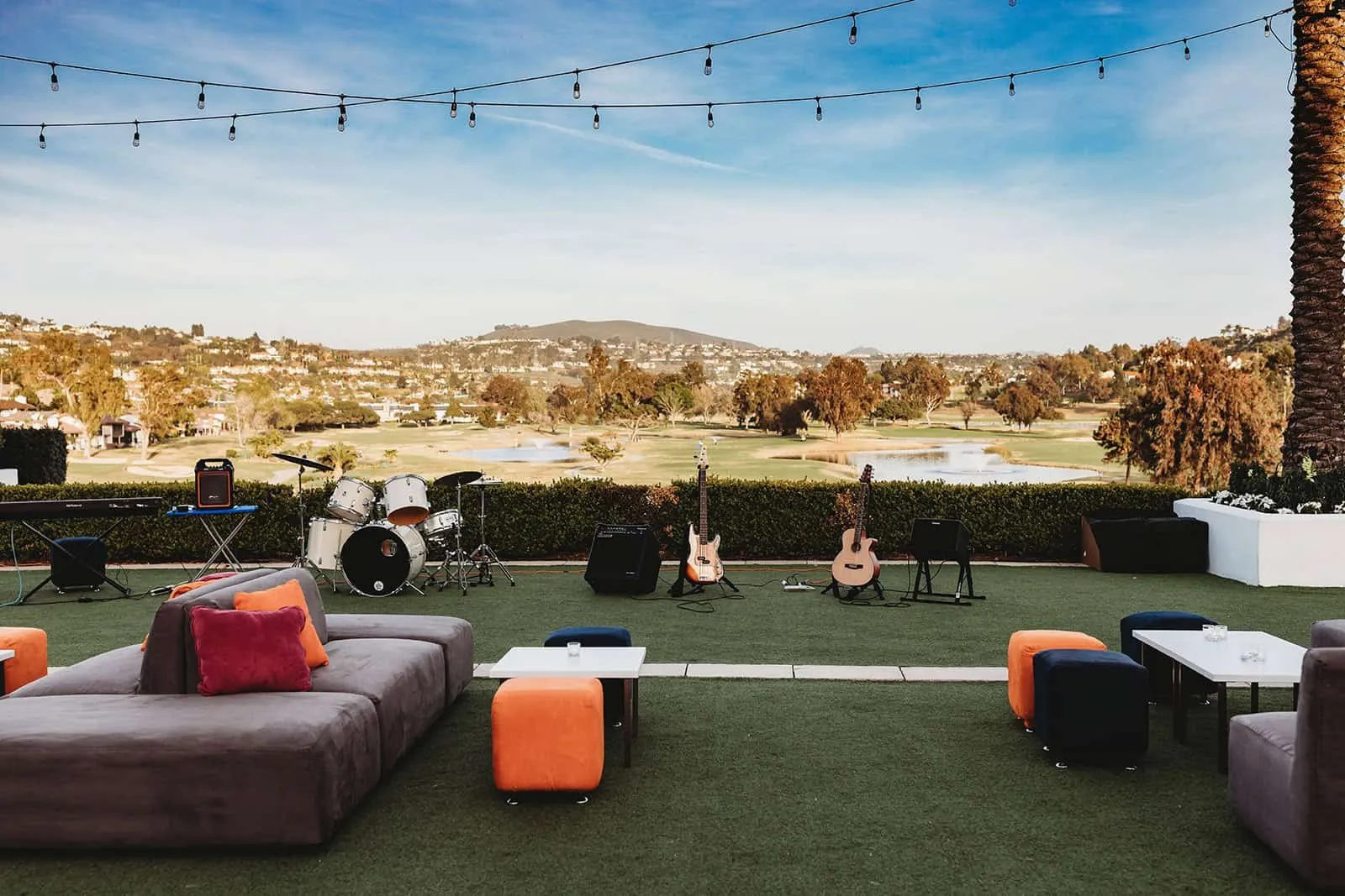 Outdoor lounge seating and a band stage on a lawn under string lights at an outdoor event