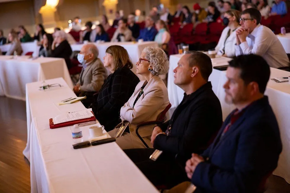 Audience seated at tables listening to a speaker at a conference