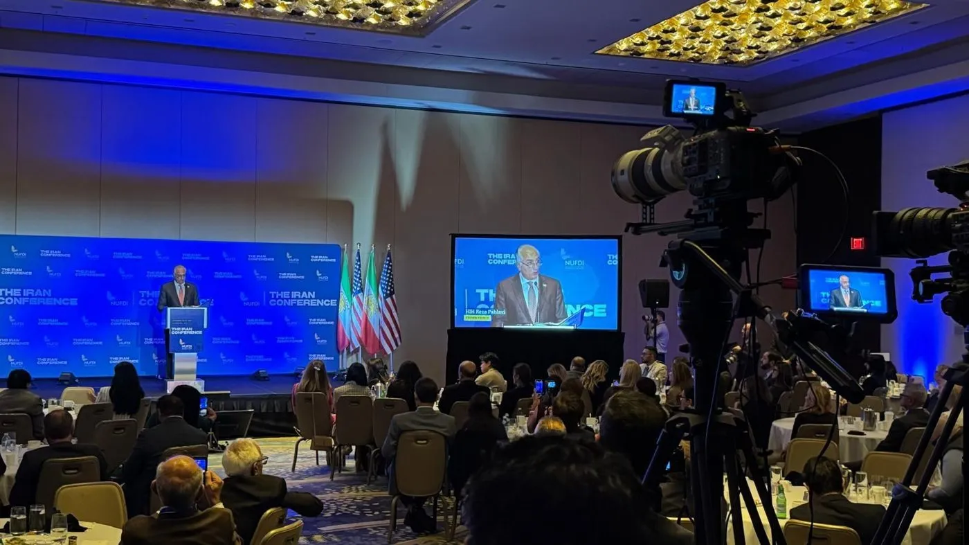 Conference ballroom with a speaker on screen and broadcast cameras in the foreground