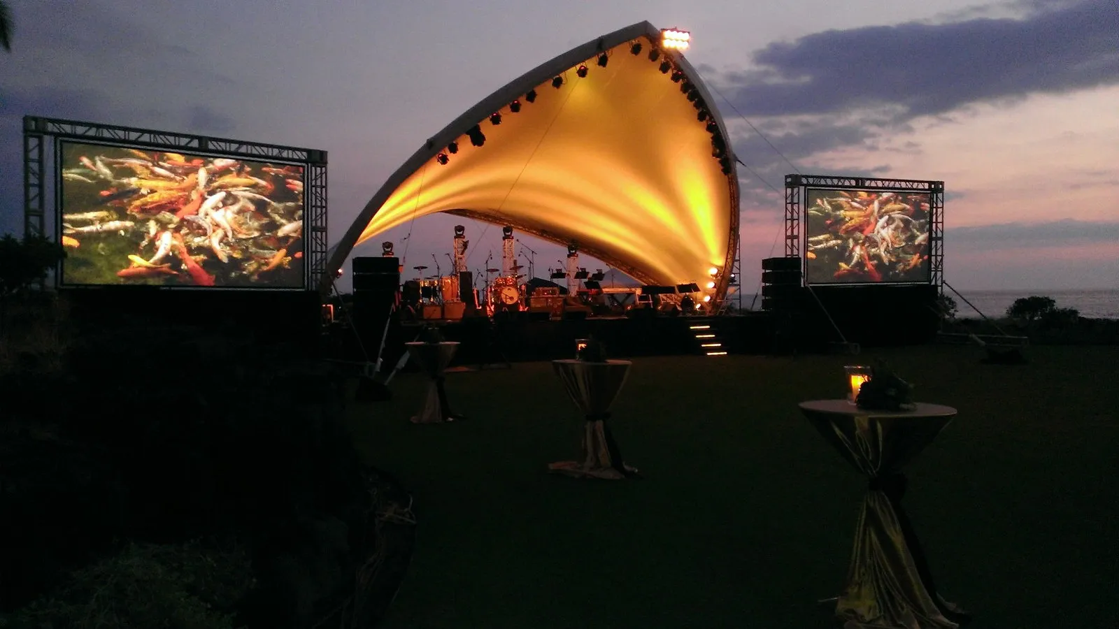 Outdoor shell stage at dusk flanked by two video screens
