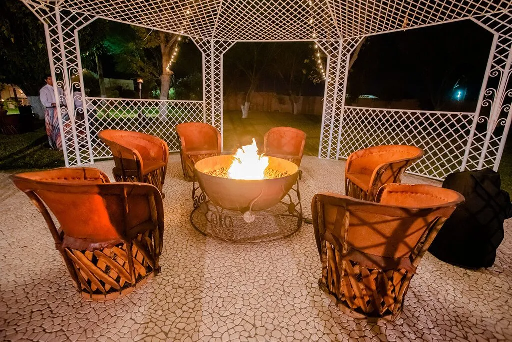 Leather chairs around a fire pit under a gazebo with string lights at night