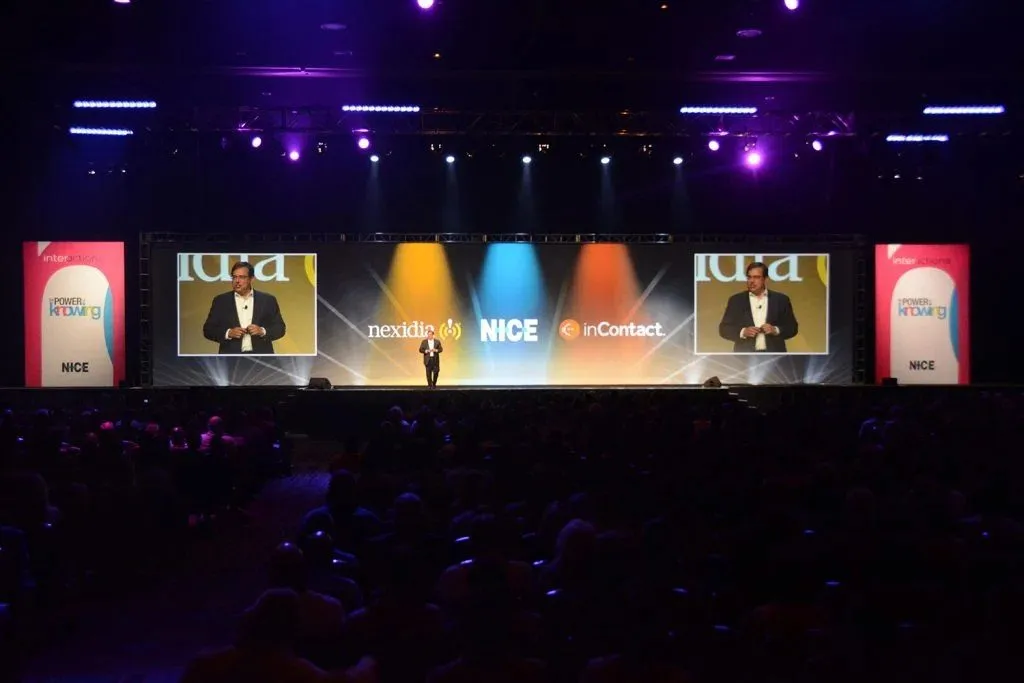 Conference stage with a speaker and large screens in front of a seated audience