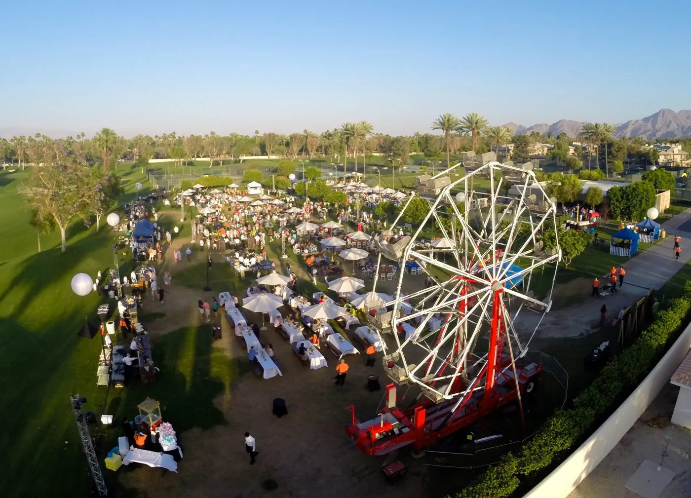 Aerial view of a large outdoor event with a ferris wheel, tables and guests on a resort lawn