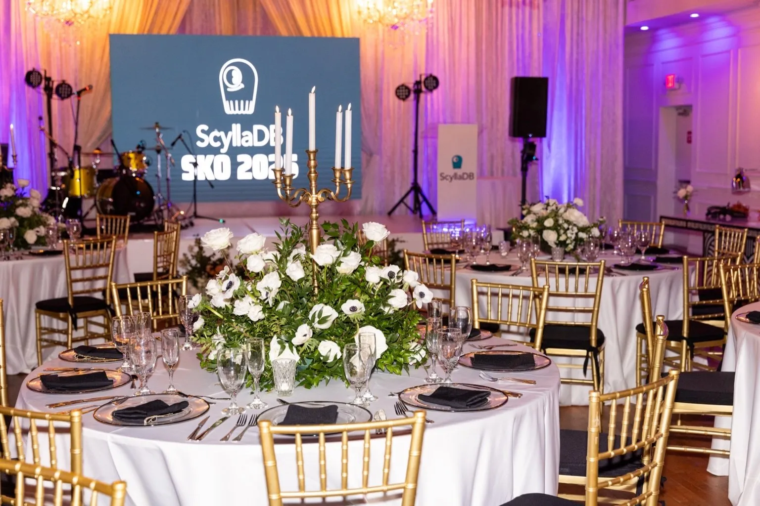 Round banquet tables with floral centerpieces and a branded screen at a corporate gala dinner