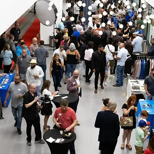 Crowd of attendees walking an expo floor between exhibitor tables