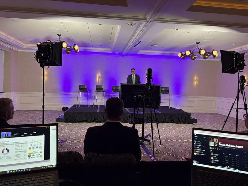 Crew at a camera and monitor position facing a lit stage with a presenter