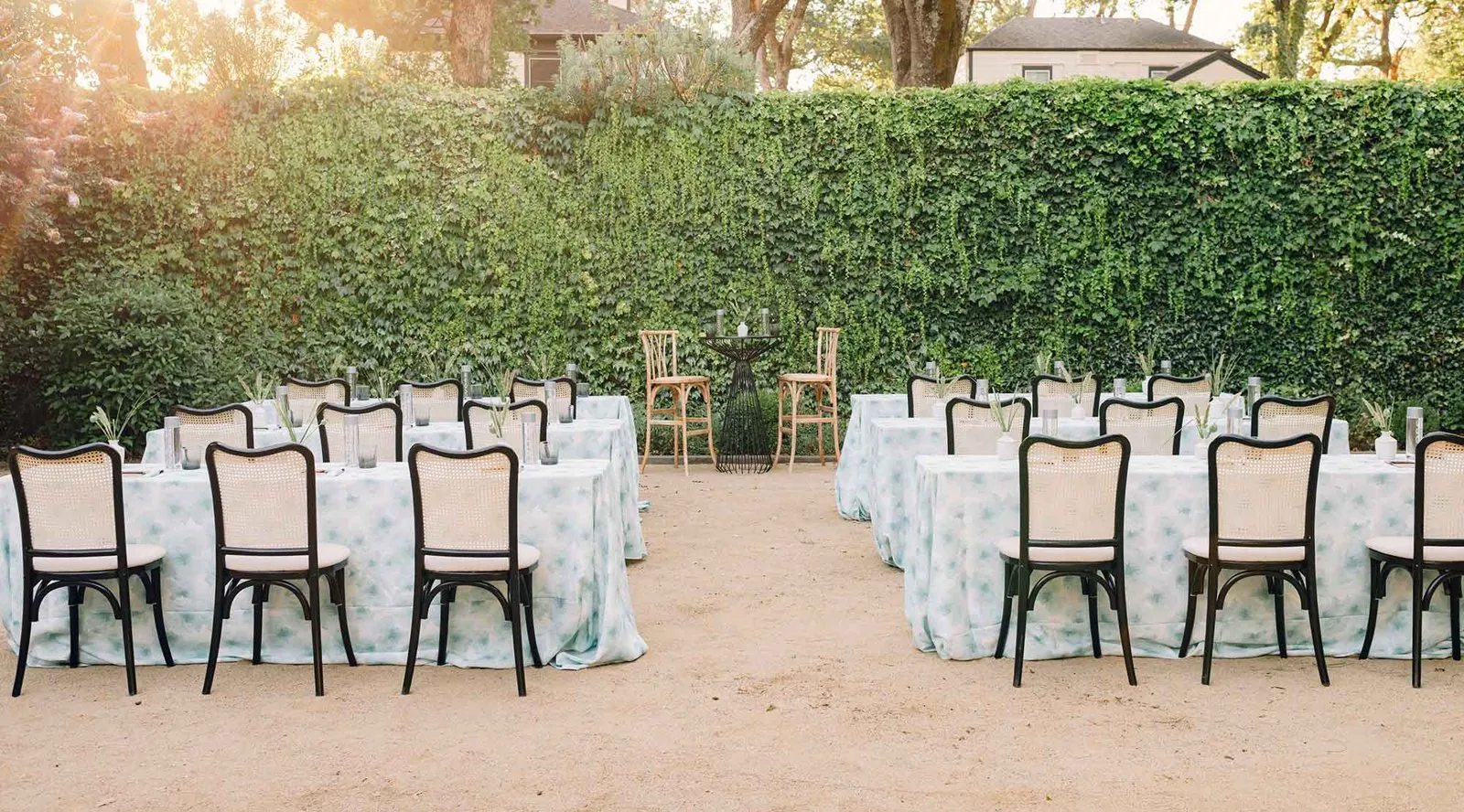 Outdoor dinner tables set beneath a tall hedge