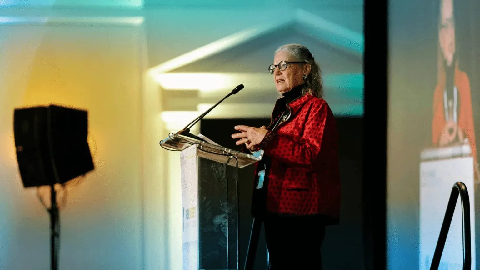 Speaker presenting at a podium on a lit stage during a corporate conference