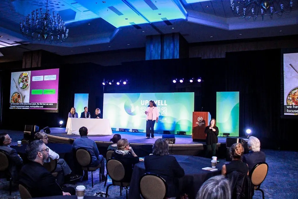 Conference panel on a lit stage with attendees seated in the ballroom