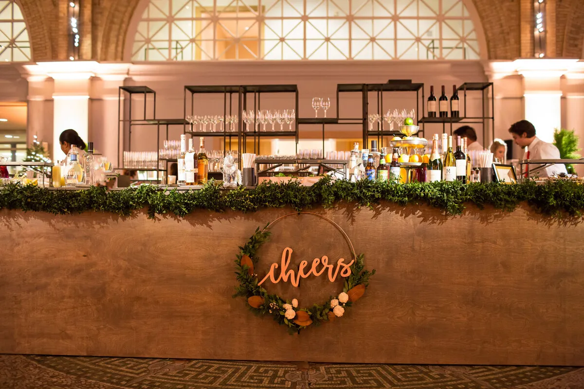 Holiday party bar with greenery garland and a cheers sign