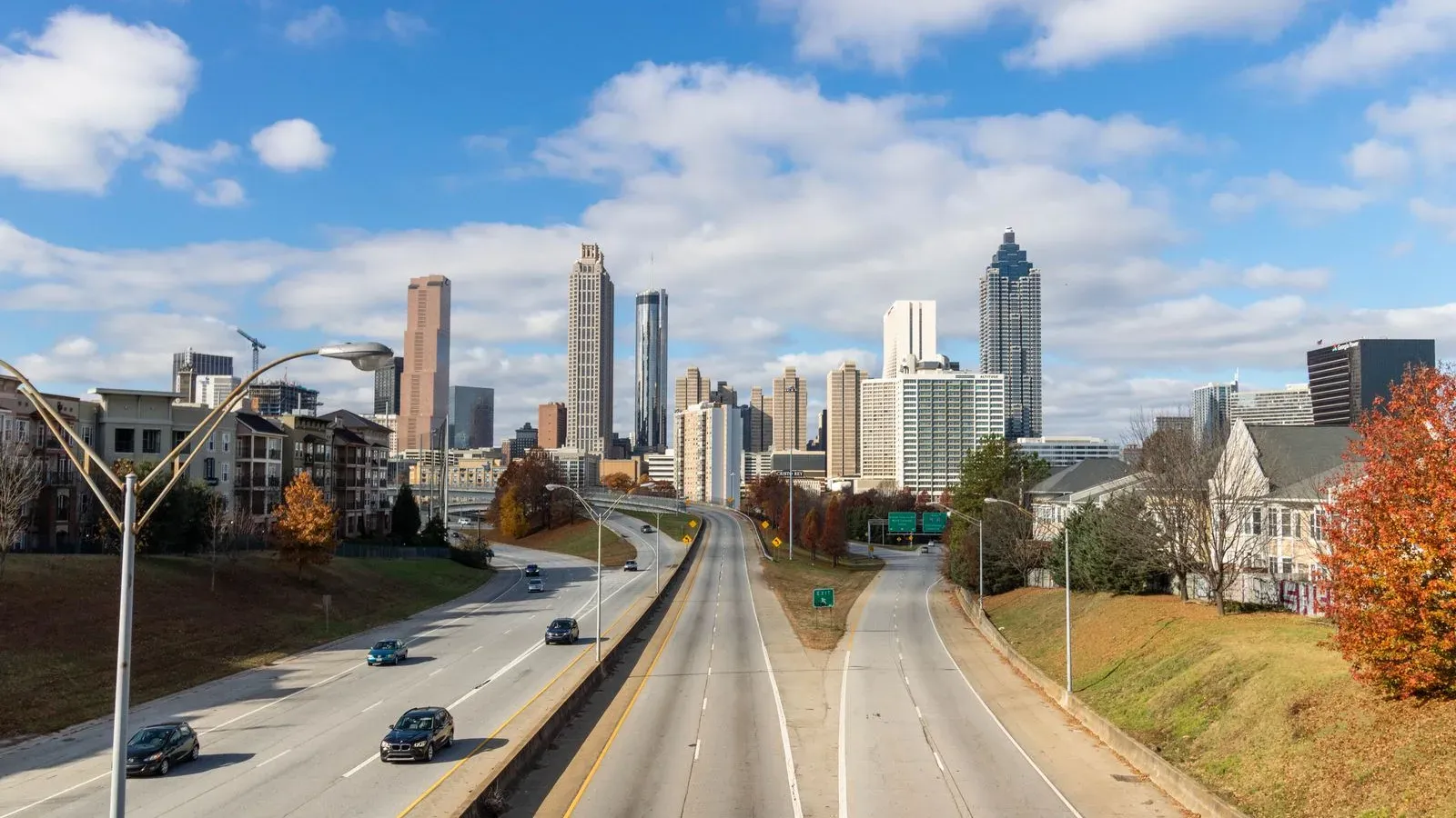 A highway leading toward the Atlanta skyline under a bright sky with clouds