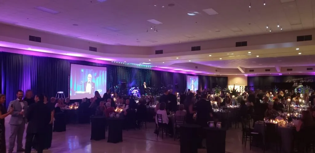Evening event in a ballroom with purple uplighting and a large screen
