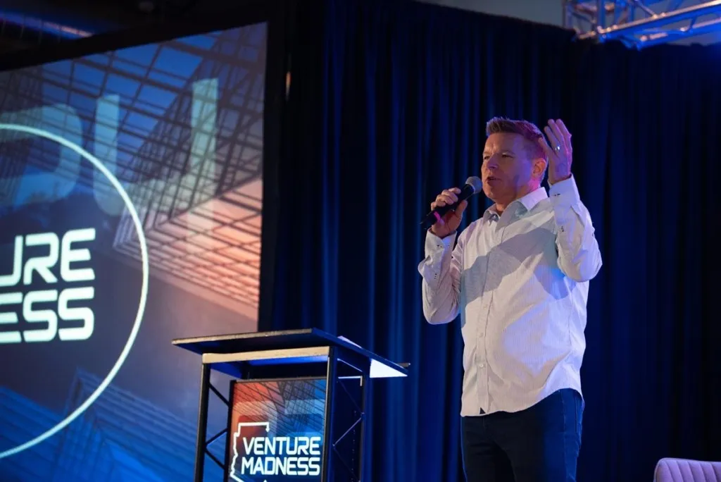 Speaker on stage in front of an LED wall at Venture Madness 2024