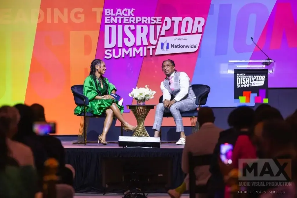 Two speakers in conversation on a colorful conference stage with an audience