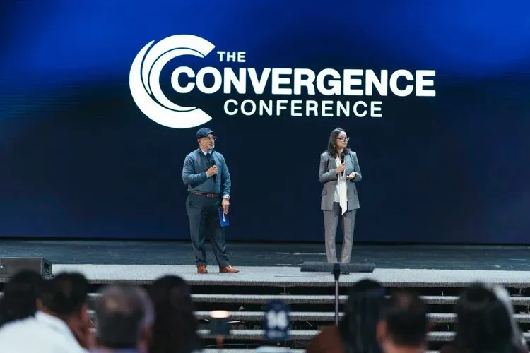 Two speakers on stage in front of a large conference logo screen