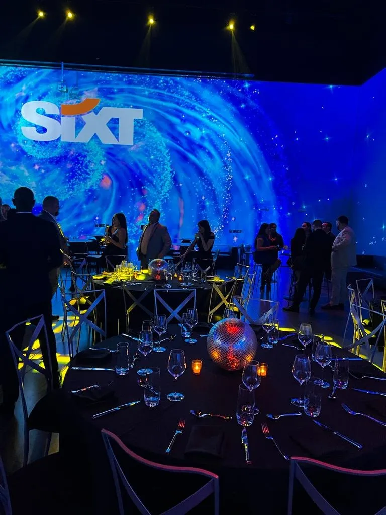 Evening event space with a large projected logo and guests seated at dinner tables