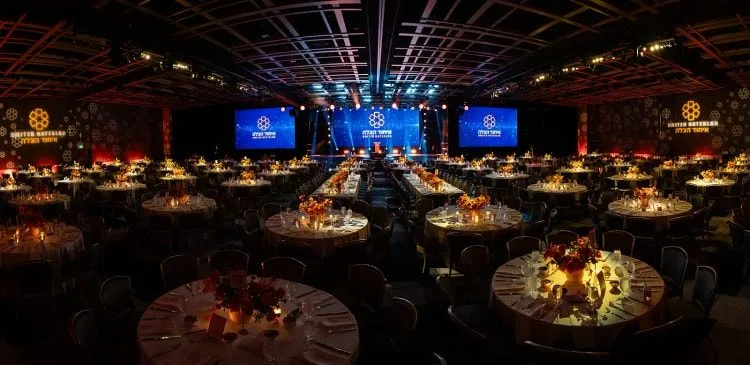 Dark ballroom with round tables and large screens set for a company dinner