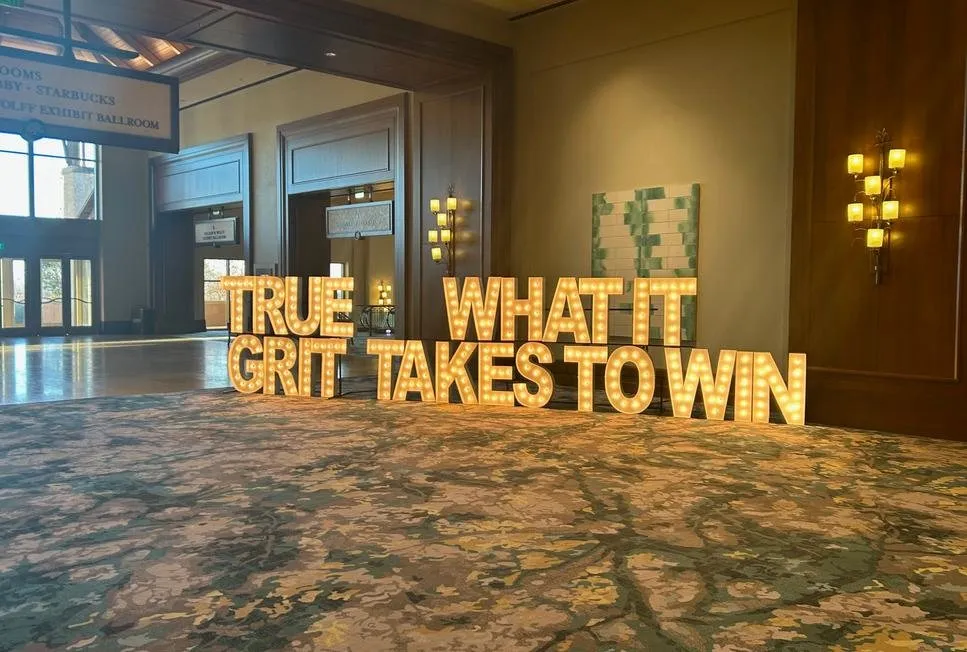 Lit letters reading True Grit, What It Takes to Win, in a hotel foyer