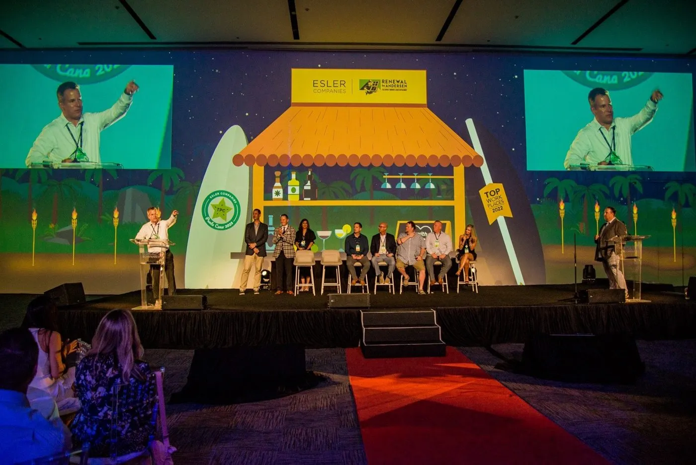 Speakers on a branded stage with large screens at a corporate event