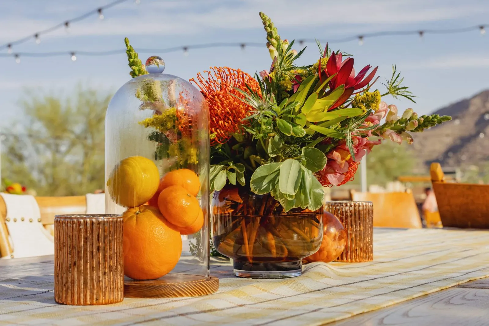 Long table with a fruit and flower centerpiece set up outdoors under string lights
