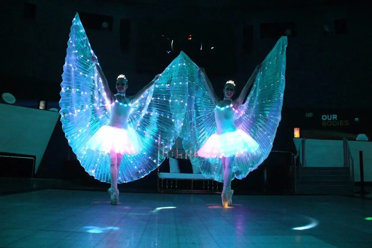 Two performers with glowing wings on a dark stage