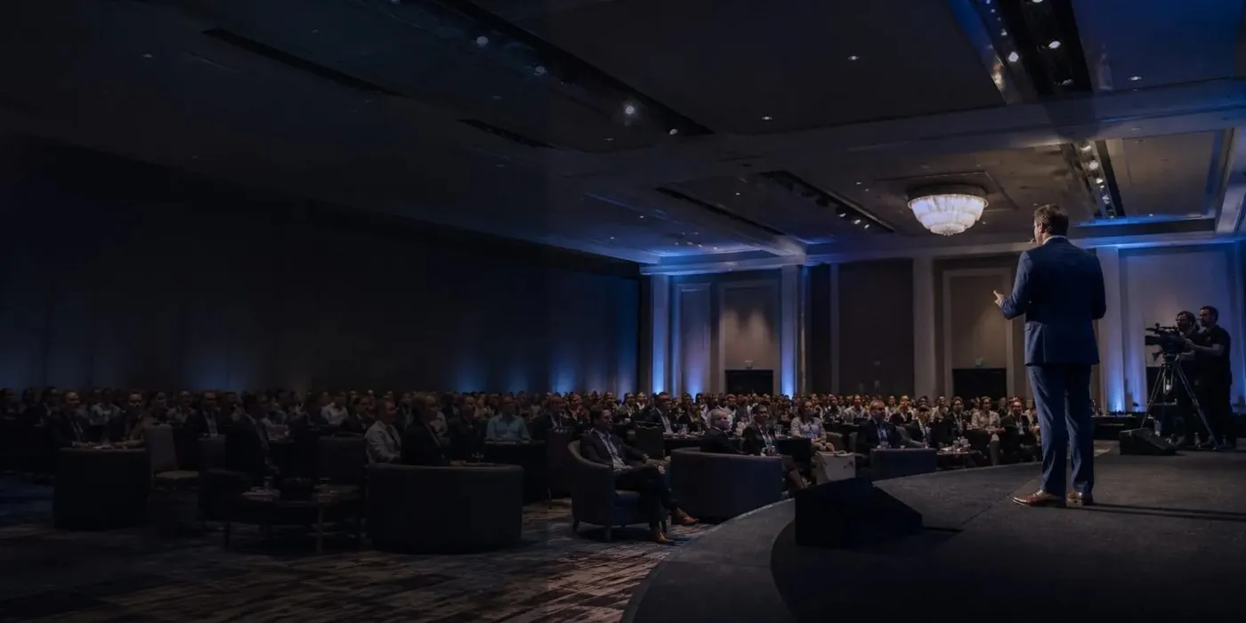 Speaker presenting to a seated audience in a blue lit conference general session