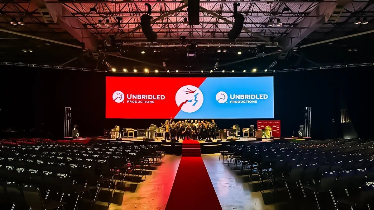 Conference hall with a red carpet aisle, chairs and a stage with large screens