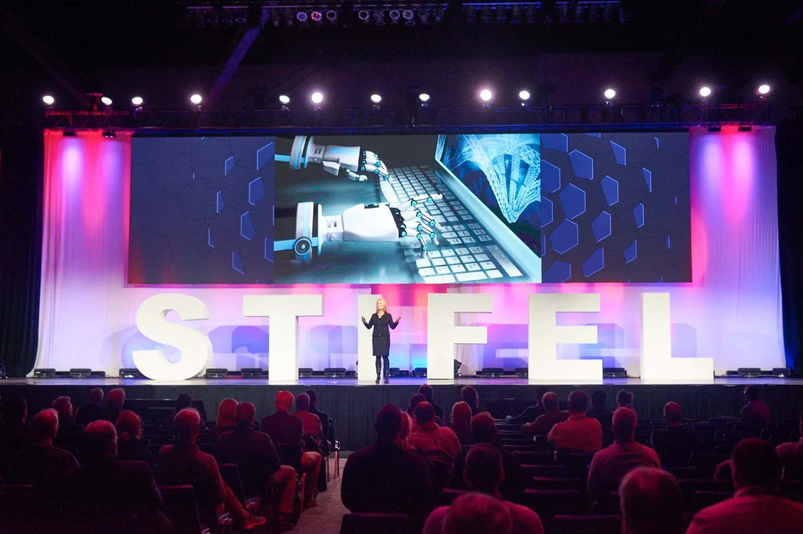 Large lit STIFEL letters on stage in front of a conference audience