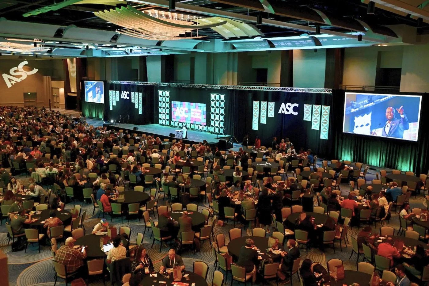 Large conference hall with an audience facing a wide stage and screens