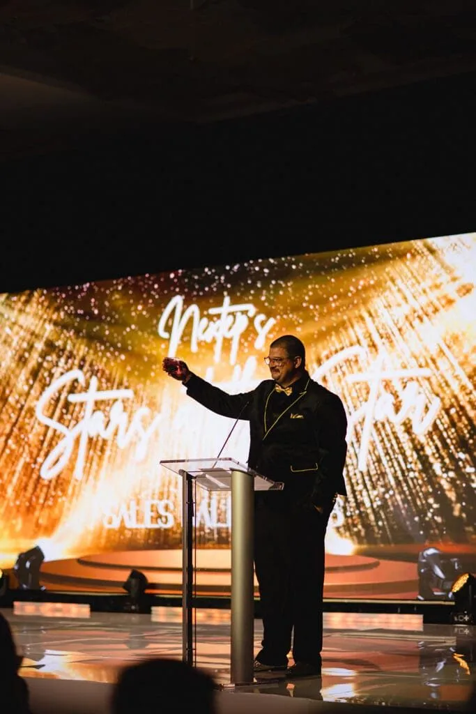 Speaker on a lit stage in front of a large video wall