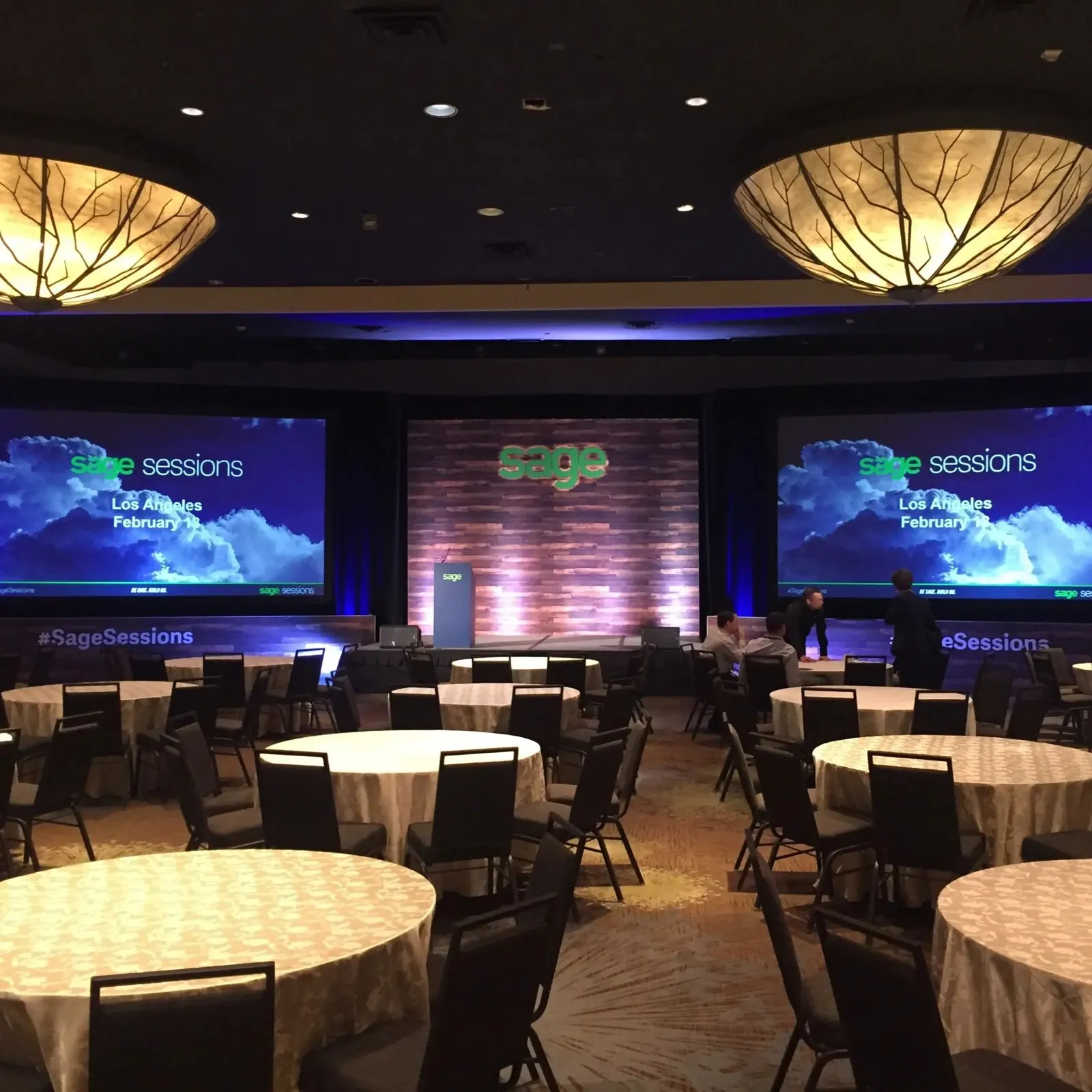 Ballroom general session with three screens, staging and round tables