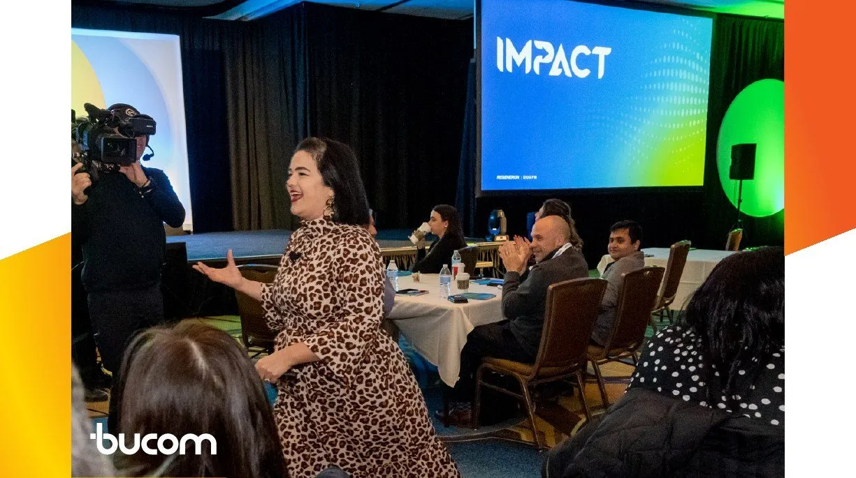 Speaker presenting on stage with a camera crew and large screens at a corporate event