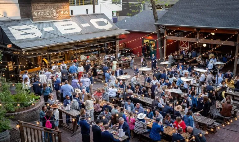 Attendees at long tables on a barbecue restaurant patio during a leadership conference evening