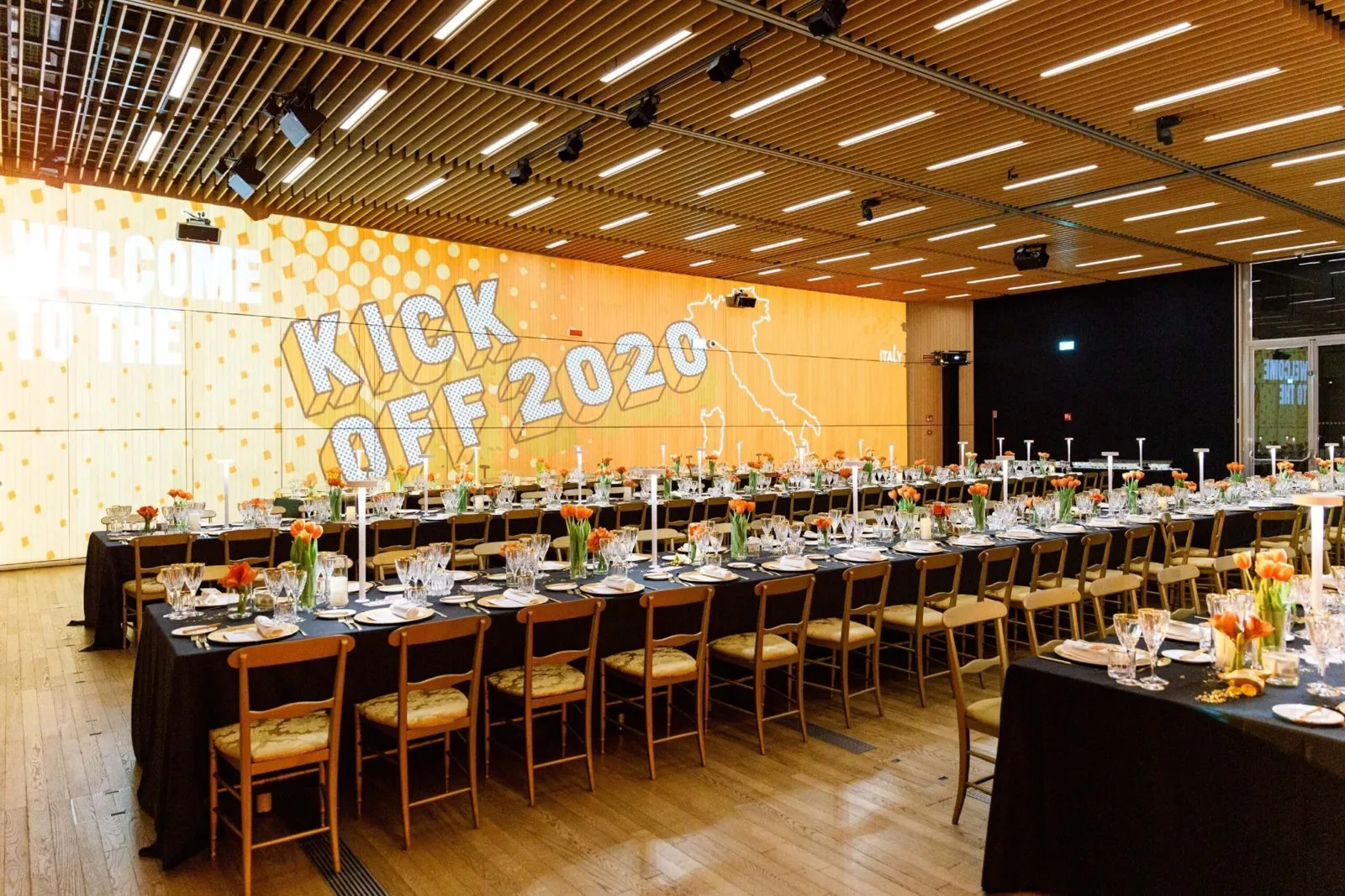 Long banquet table in a wood-paneled venue beneath a lit Kick Off 2020 sign
