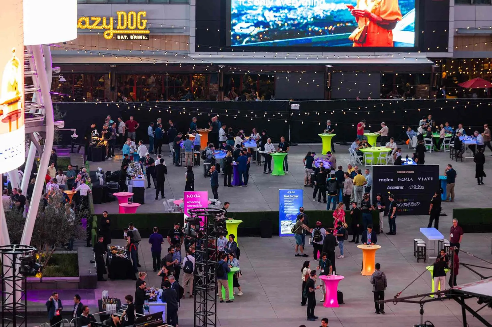 Attendees on an indoor arena floor with stage screens at a large corporate event