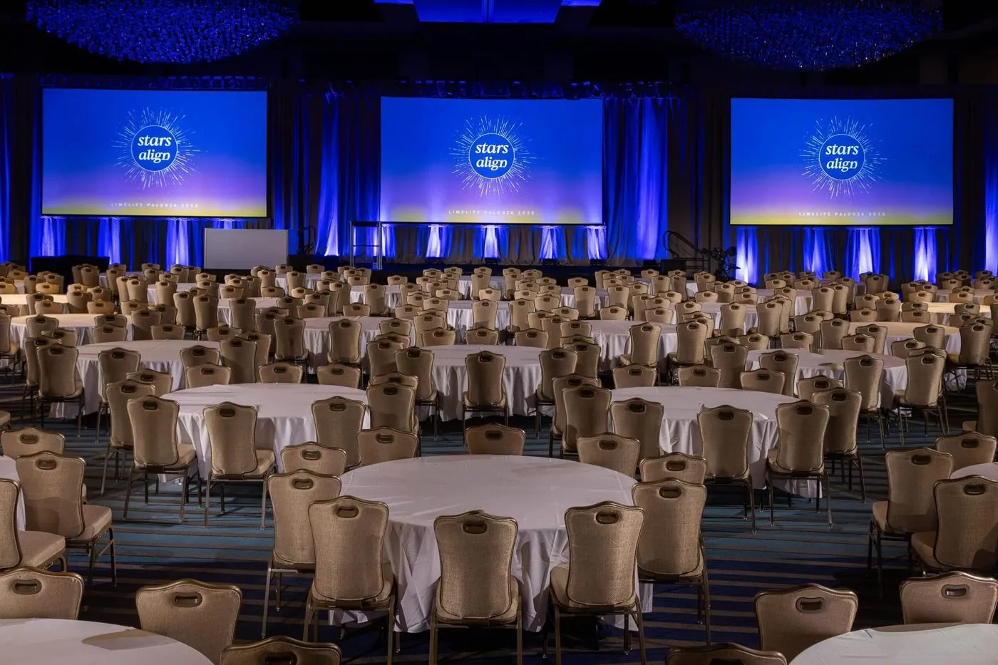 Ballroom set with round tables and three large stage screens