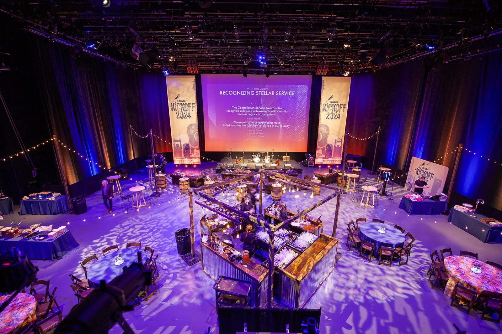 Ballroom set for an evening event with purple lighting, banners and a stage screen
