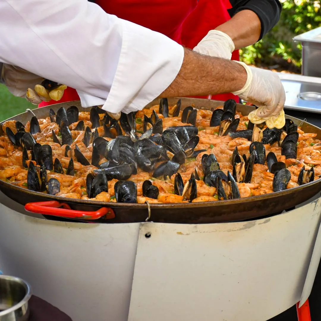 Seafood paella with mussels and shrimp being prepared in a large pan at a food station, Impact 100 Men charity event, May 2024