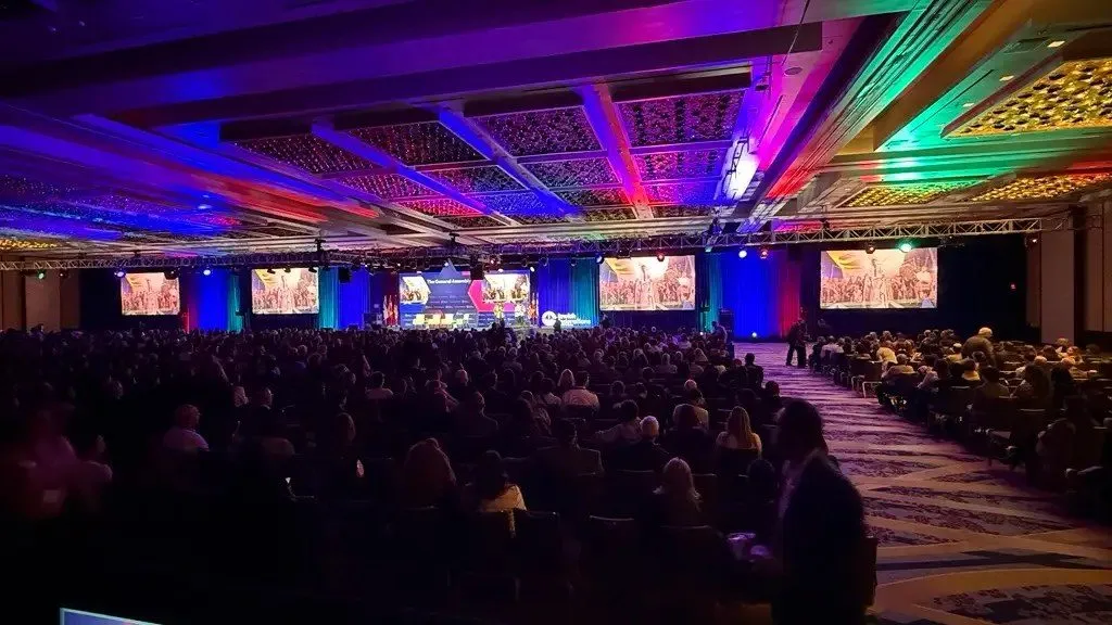 Conference ballroom with colorful ceiling lighting and rows of seated attendees