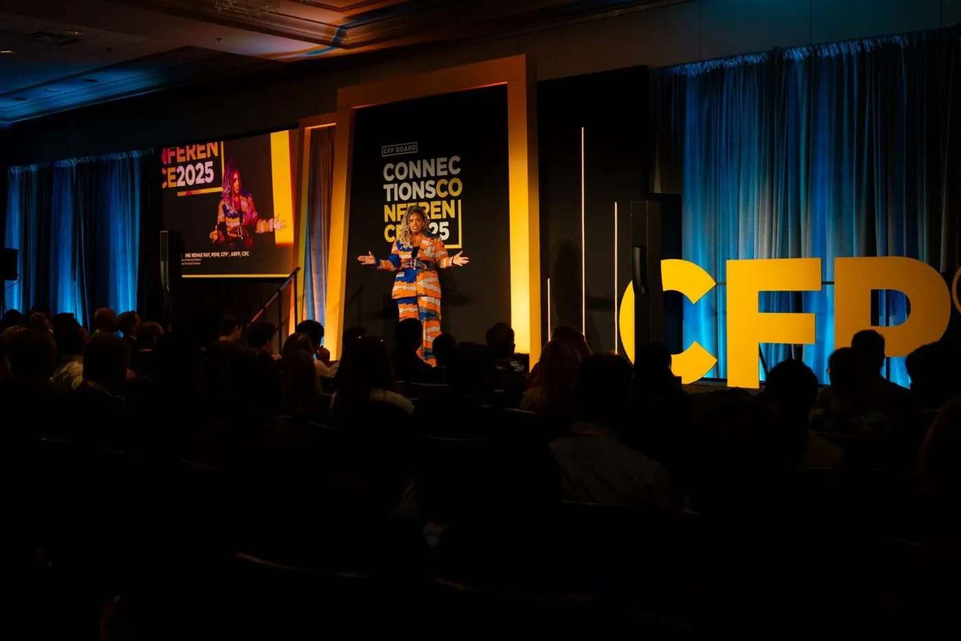 Keynote speaker on a conference stage with a large illuminated sign