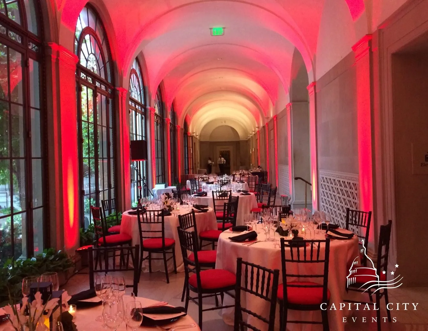 Arched corridor with red lighting and round tables set for a group dinner