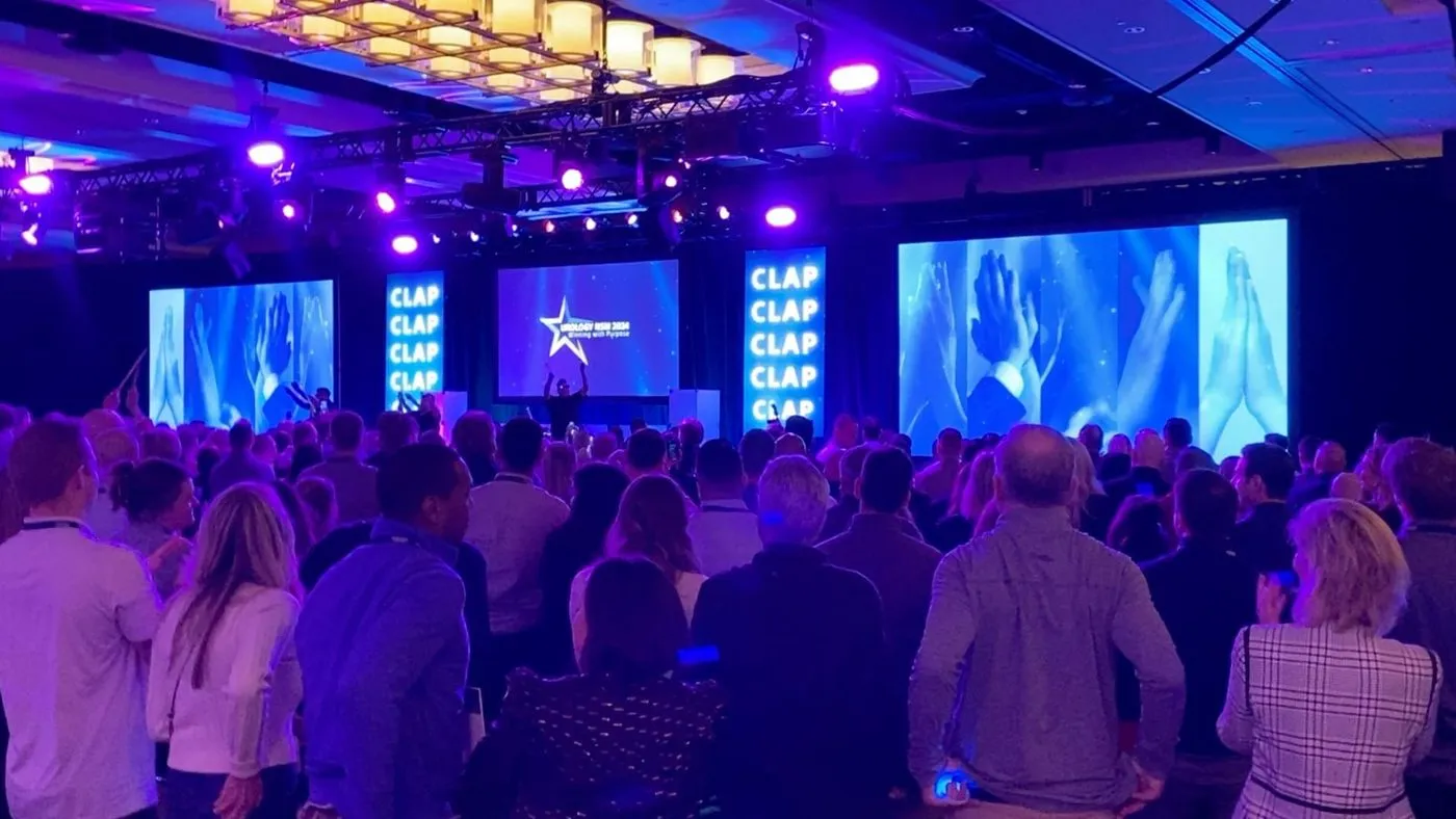 Audience standing in front of blue lit LED screens at a corporate meeting
