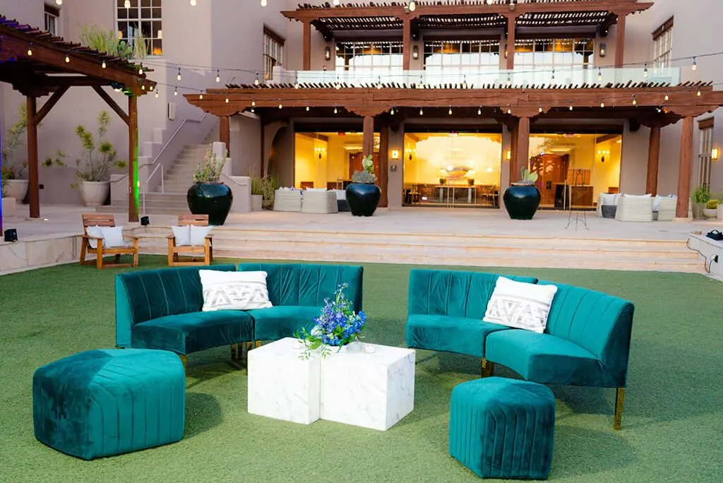 Teal sofa lounge with ottomans set on a lawn in front of a resort patio